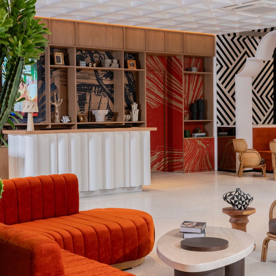 Modern lounge with vibrant orange and beige furniture, geometric black and white wall patterns, and a wooden shelving unit adorned with art pieces.