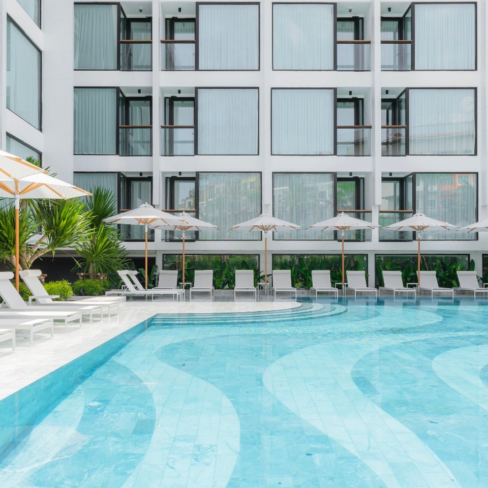 Modern hotel poolscape with clear turquoise water, surrounded by white lounge chairs and umbrellas. The background shows a sleek building facade. Relaxing vibe.