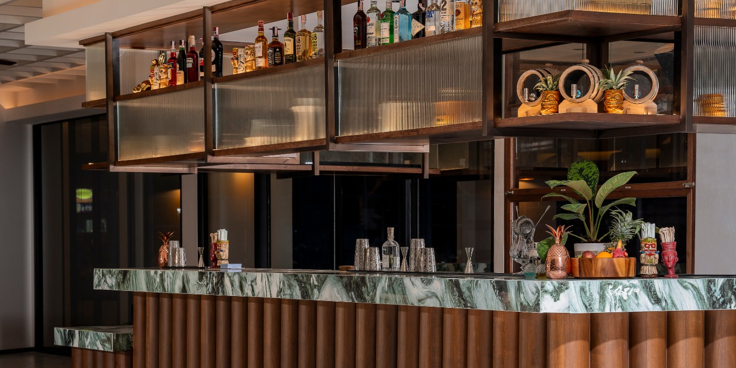 A modern bar with a luxurious marble countertop and wooden paneling. Shelves above display various liquor bottles. The ambiance is elegant and inviting.