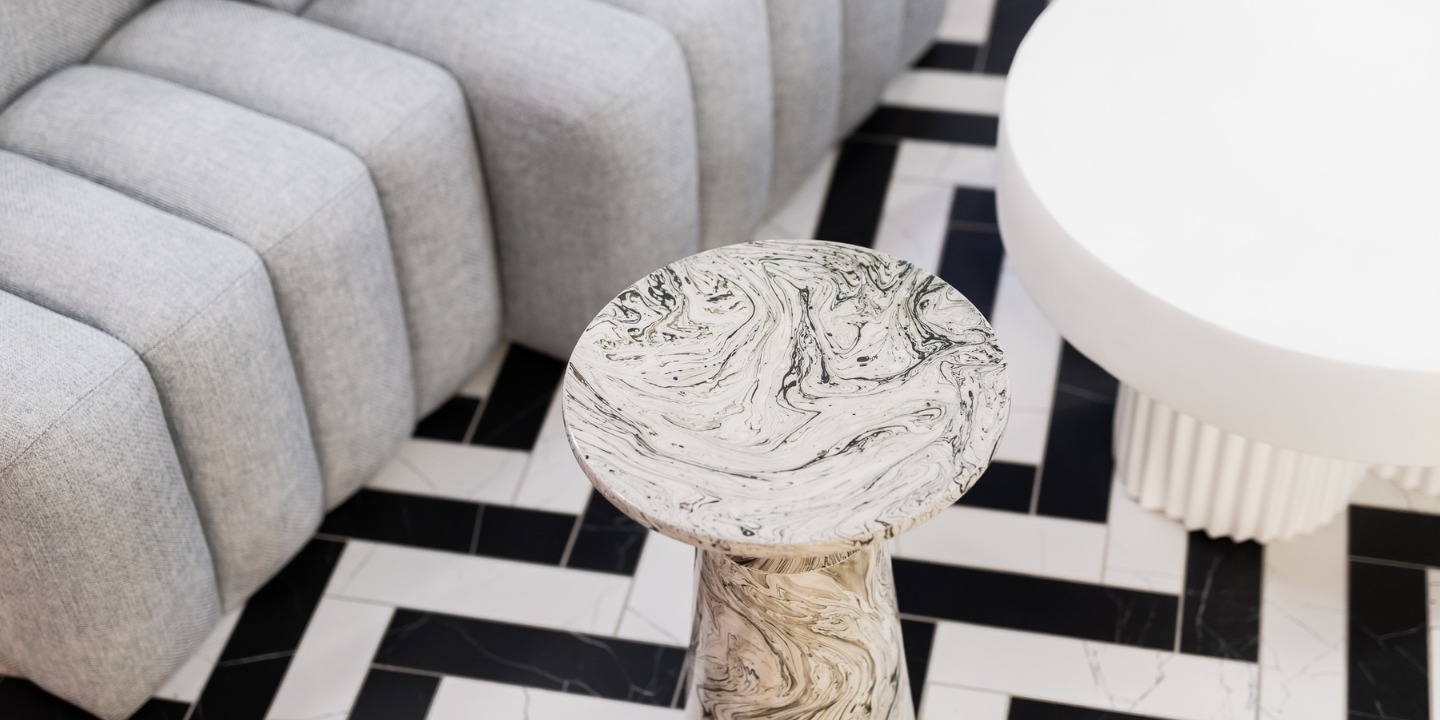 Stylish marble side table with a swirling black and white pattern, set against a geometric floor and a plush grey sofa.